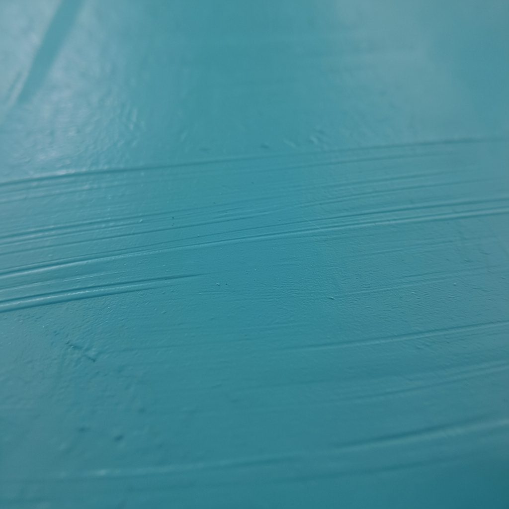 Extreme close-up of matte painted metal in muted teal, with a smooth, even finish and faint horizontal brush strokes visible